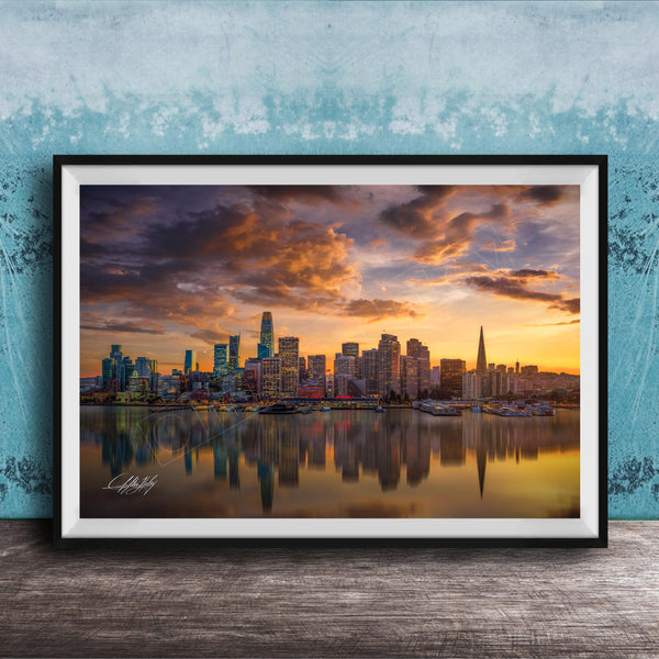 A framed photograph depicting a city skyline at sunset, with the city's buildings reflected in the water below.