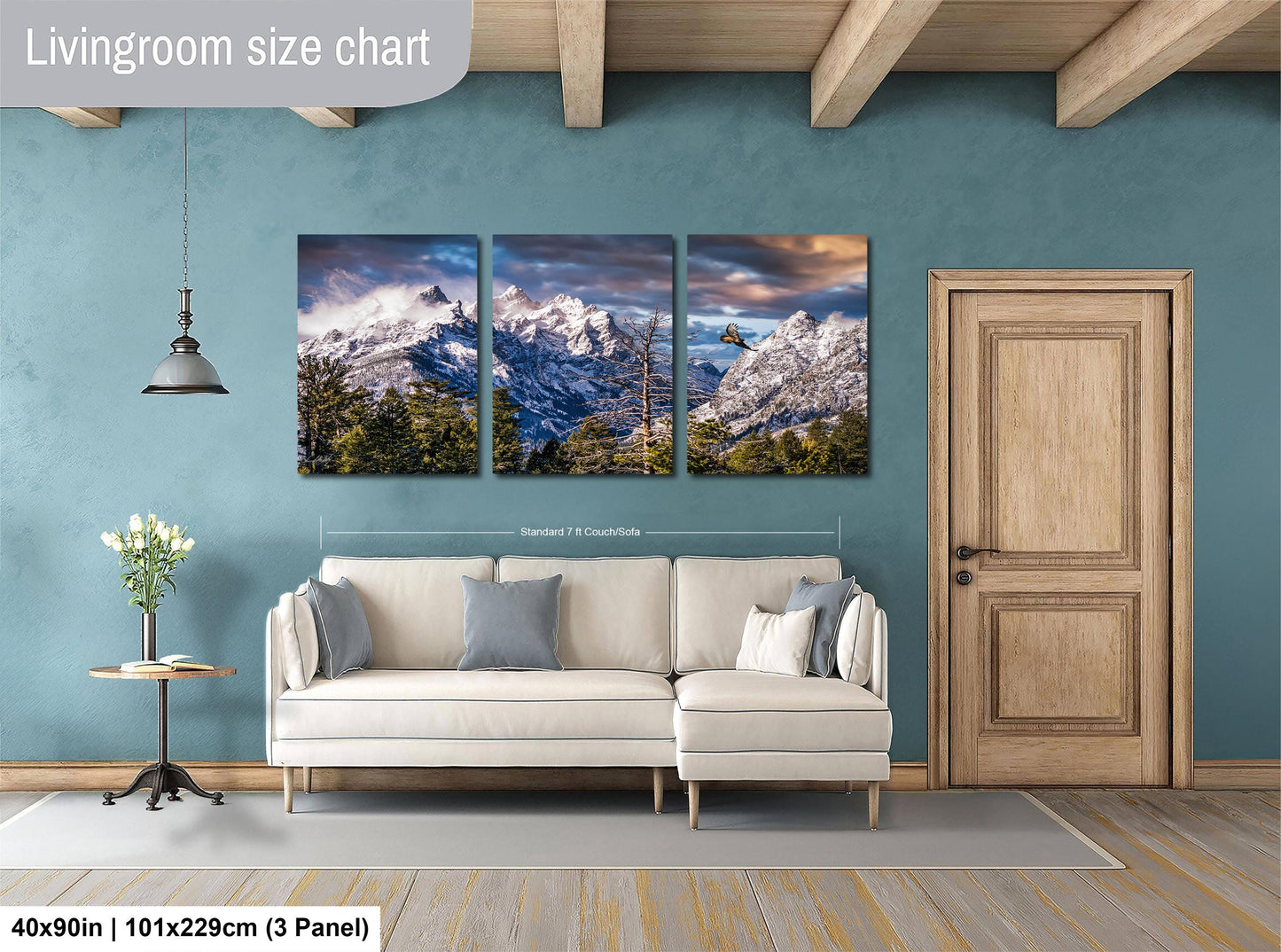 The image is a living room with a large wall art depicting a scenic mountain landscape. The wall art is composed of three panels, each showcasing a different part of the mountain range. The living room has a white sofa and a wooden door, creating a cozy and inviting atmosphere.