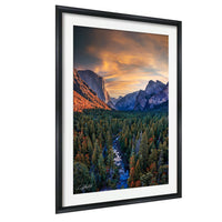 The image is a framed photograph of a scenic mountain landscape with a river flowing through a forested valley. The mountains are covered in snow, and the sky is filled with vibrant colors, creating a breathtaking natural scene.