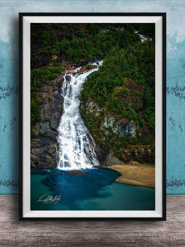 A framed photograph of a waterfall cascading down a rocky cliff surrounded by lush greenery, with a blue-green body of water below.