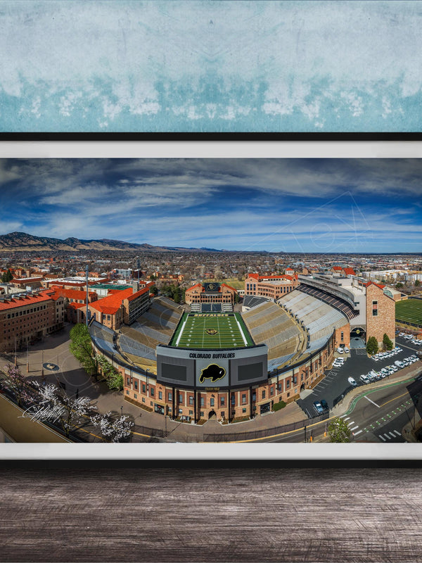 The image is a framed photograph of a football stadium, likely a college or university stadium, with a cityscape in the background.