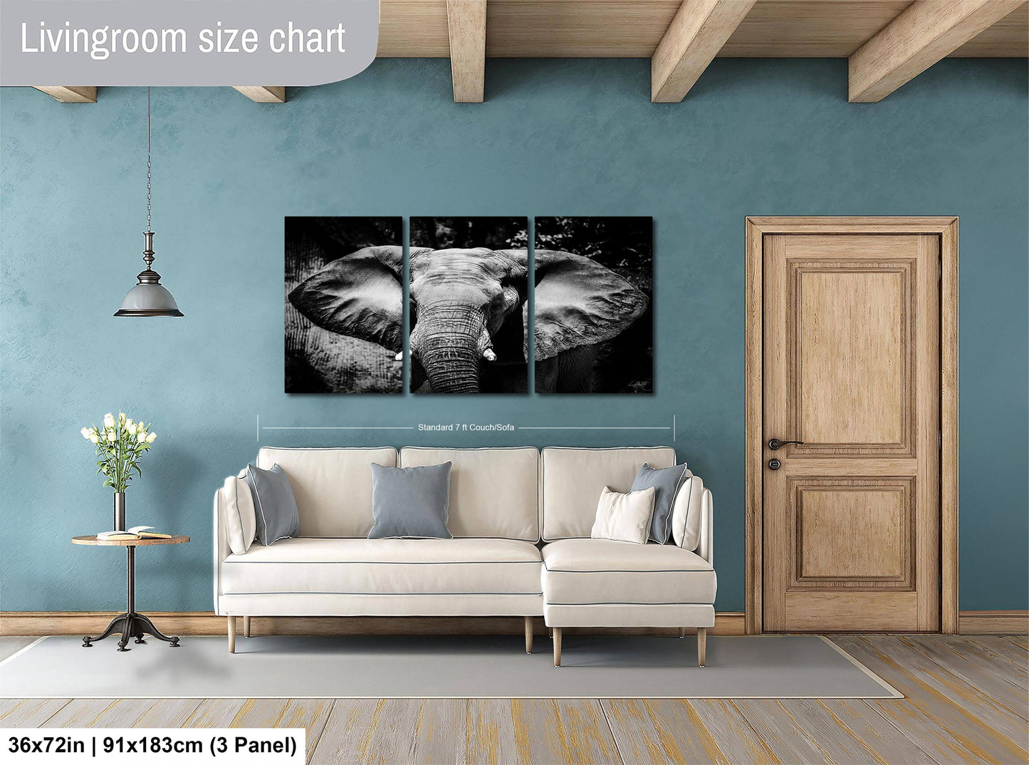 The image is a living room with a large wall art piece depicting an elephant. The living room has a white sofa, a wooden door, and a wooden beam ceiling. The wall art is a collage of three separate images, and the dimensions of the wall art are 36 inches by 91.5 centimeters by 3 panels.