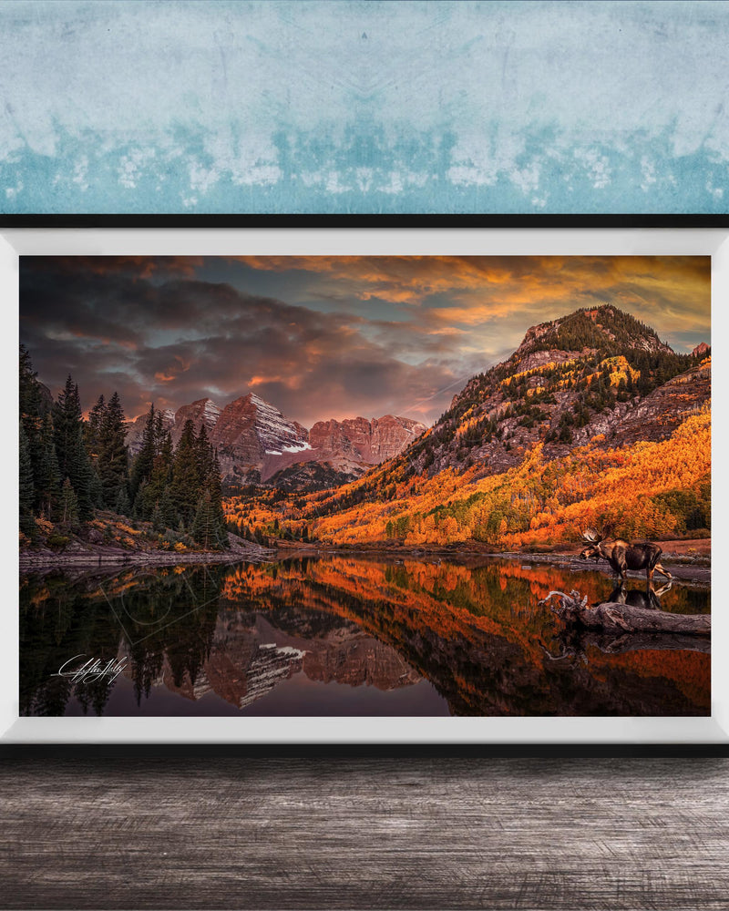 The image is a framed photograph depicting a serene mountain landscape with a lake, trees, and mountains in the background, reflecting the vibrant colors of the sky.