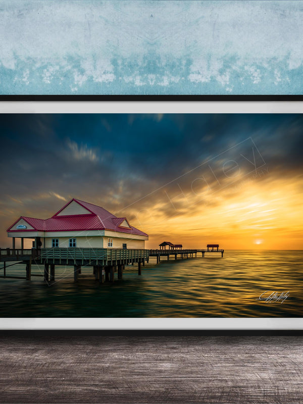 A framed photograph depicting a serene pier scene at sunset, with a red-roofed building and a wooden pier extending into the calm waters.
