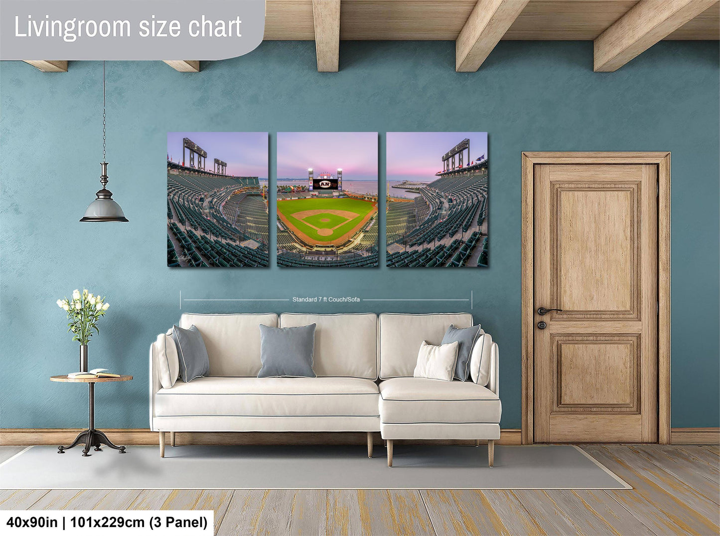 The image is a living room with a large wall-mounted painting depicting a baseball stadium. The painting is divided into three panels, each showing different aspects of the stadium, such as the field, seating, and scoreboard. The painting is framed in a white frame and hangs on the wall, which has a wooden door and a white sofa.