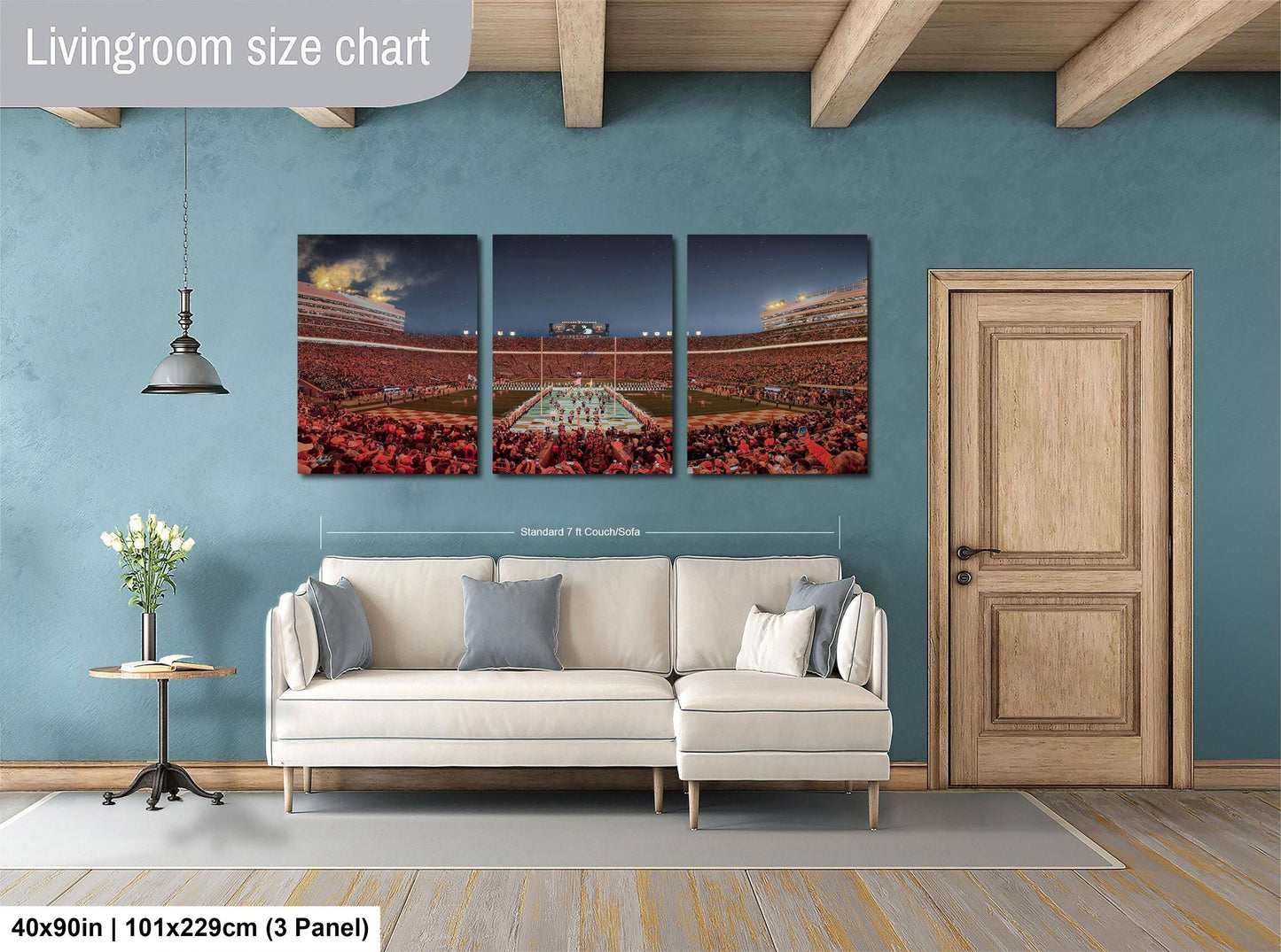 The image is a living room with a large wall art depicting a stadium scene. The wall art is divided into three panels, each showing different parts of the stadium. The living room has a white sofa and a wooden door, and the floor is covered with a gray rug.