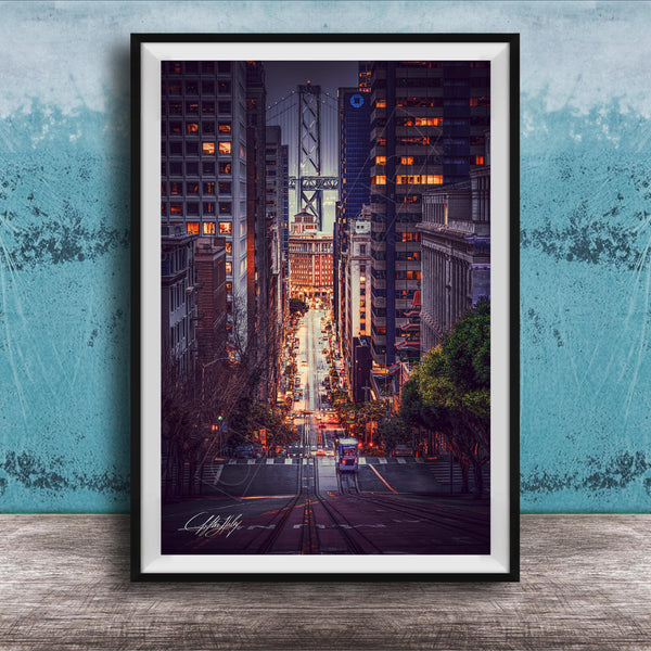 A framed photograph depicting a city street at night, with tall buildings and a bridge in the background. The street is illuminated by streetlights and the glow of the buildings, creating a vibrant and dynamic scene.
