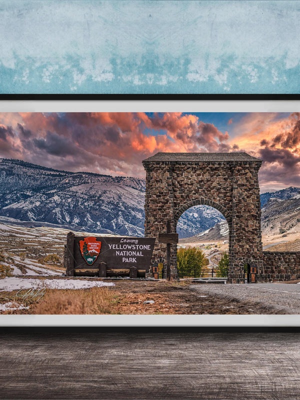 A framed photograph of the iconic Arch of the Sun, a historic stone monument located in Yellowstone National Park, with a breathtaking mountain landscape in the background.