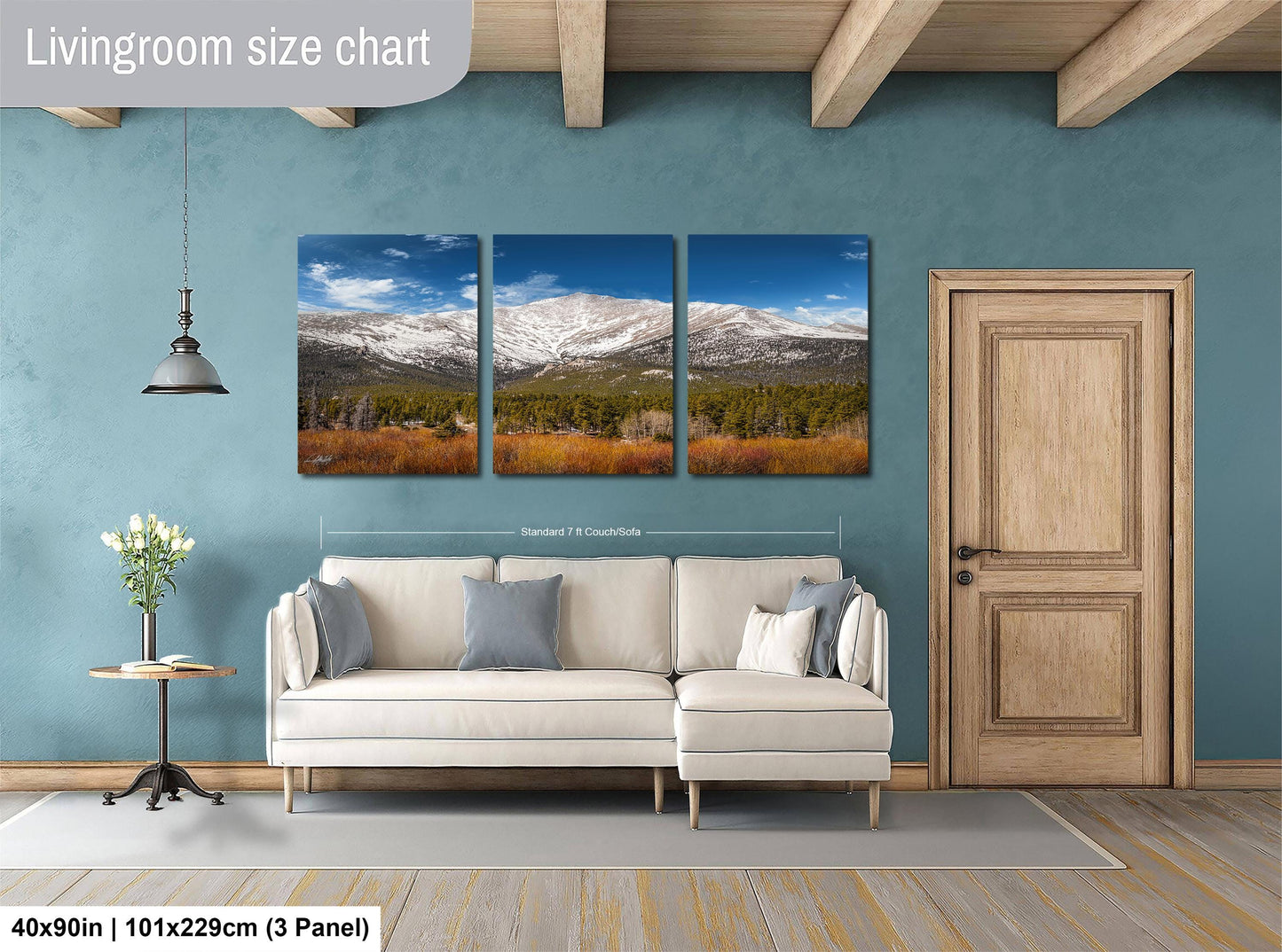 The image is a living room with a large, three-panel landscape painting hanging on the wall. The painting depicts a mountain range with snow-capped peaks and a field of trees in the foreground. The room has a white sofa and a wooden door, creating a cozy and inviting atmosphere.