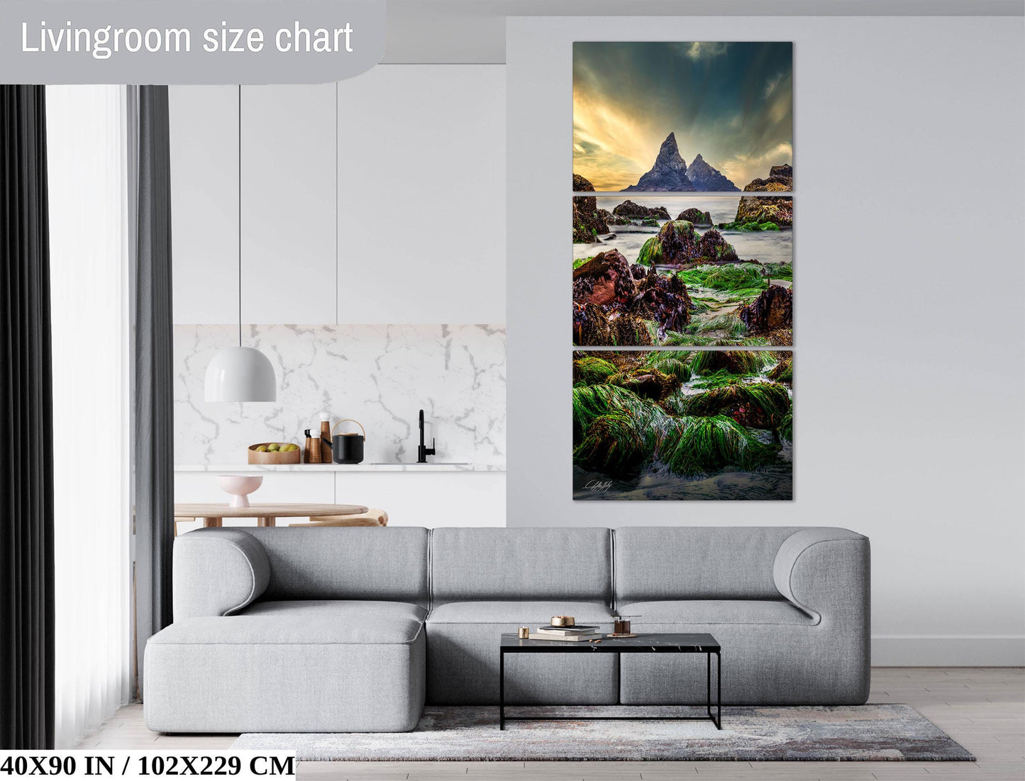 The image is a living room with a gray sofa and a coffee table in front of it. Above the sofa, there is a large painting depicting a scenic landscape with mountains and a body of water. The painting is framed and hangs on the wall, adding a decorative element to the room.