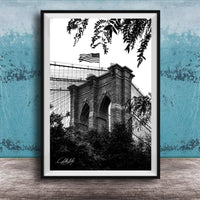 A black and white photograph of the Brooklyn Bridge, with the American flag flying atop the structure.