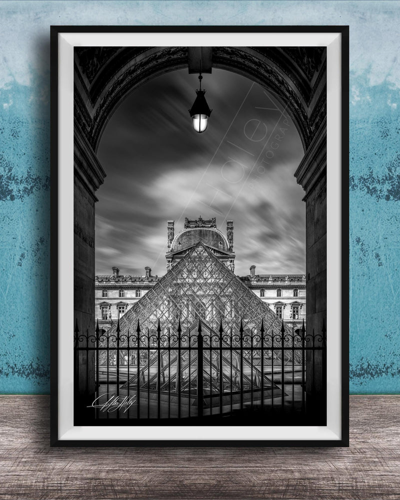 A framed black and white photograph of the Louvre Museum in Paris, France, with the iconic glass pyramid structure of the museum prominently featured.