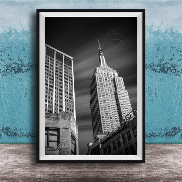 A black and white photograph of the Empire State Building, a famous skyscraper in New York City, with a blue wall in the background.