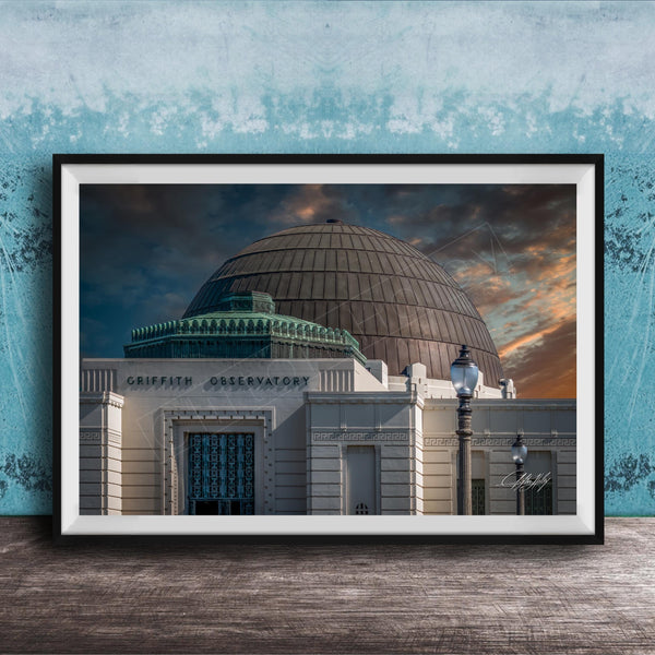 the Griffith Observatory, a large domed building with a distinctive architectural style, set against a dramatic sky with clouds and a sunset.