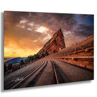 a large, steep rock formation with a winding path leading up to it, set against a dramatic sky with vibrant orange and purple hues.
