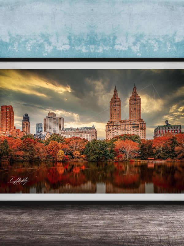 a cityscape with tall buildings and a lake in the foreground, surrounded by trees with autumn foliage.