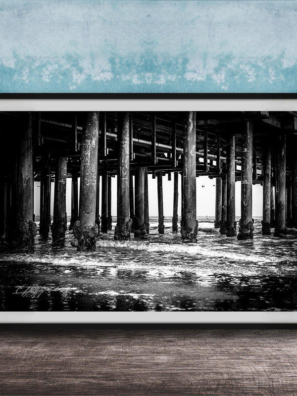 A black and white photograph of a pier with multiple columns and pillars, set against a blue textured wall.