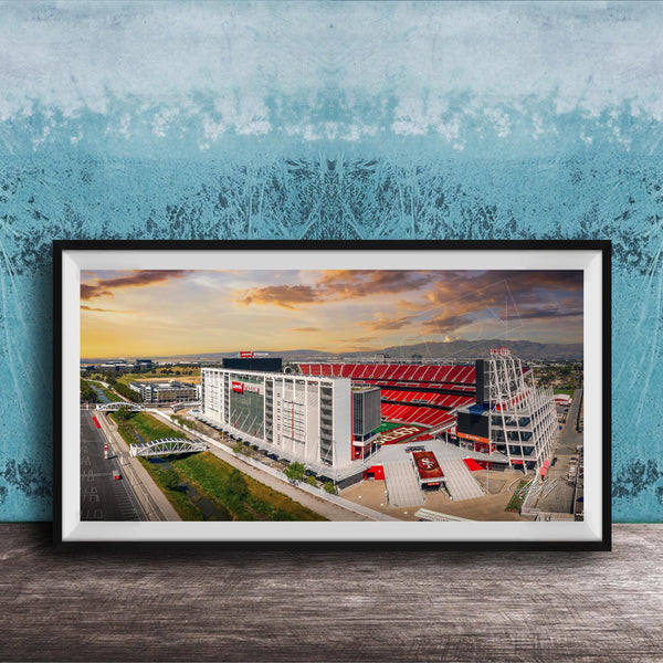 The image is a framed photograph of a large stadium with a red roof, set against a backdrop of a blue sky with clouds.