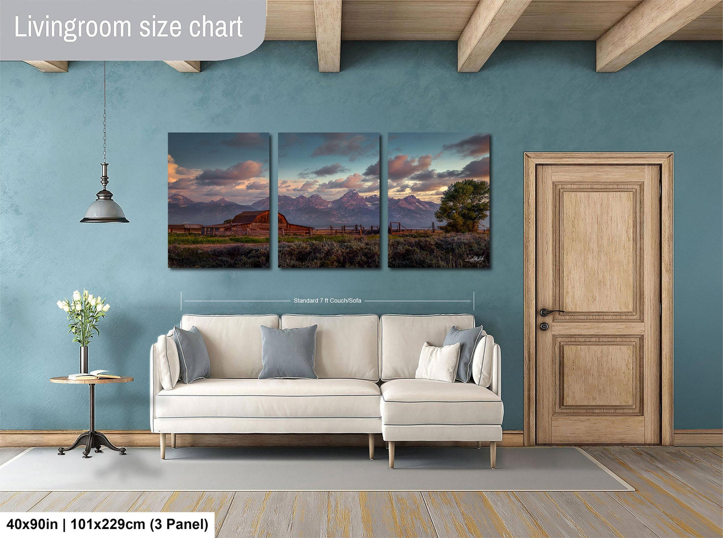 The image is a living room with a large, white sofa and a wooden door. Above the sofa, there is a triptych of landscape paintings depicting a mountain range and a sunset. The paintings are framed and hung on the wall, creating a cozy and inviting atmosphere in the living room.