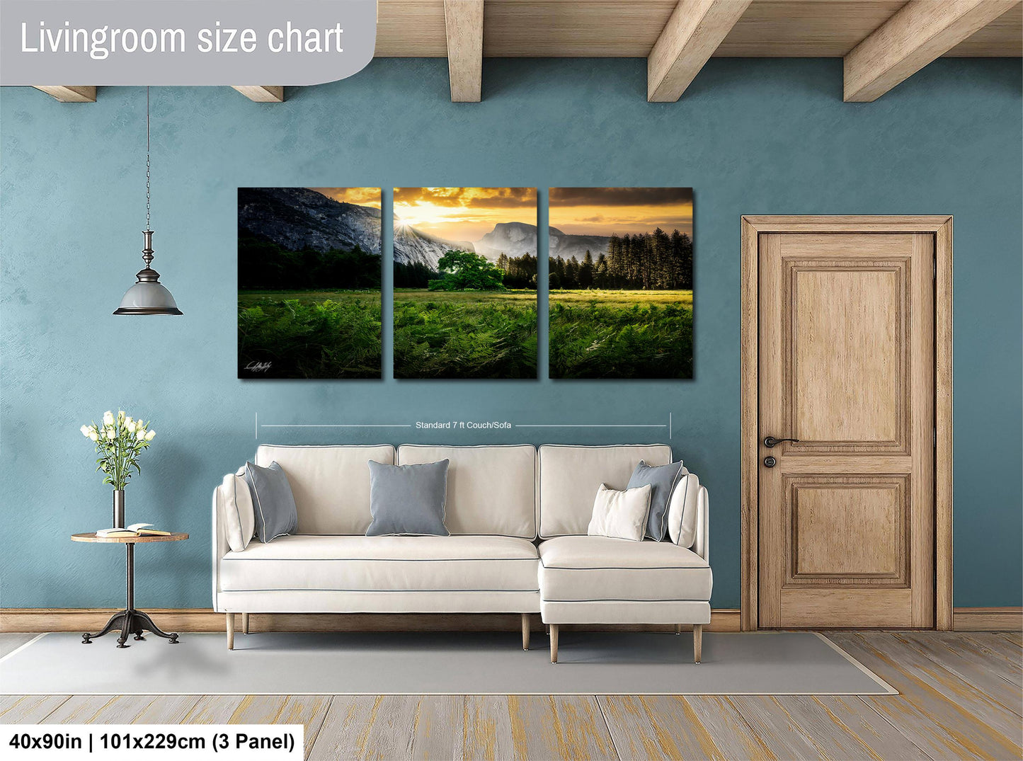 The image is a living room with a large, three-panel landscape painting hanging on the wall. The painting depicts a serene mountain landscape with a sunset over the mountains. The room is furnished with a white sofa and a wooden door, creating a cozy and inviting atmosphere.