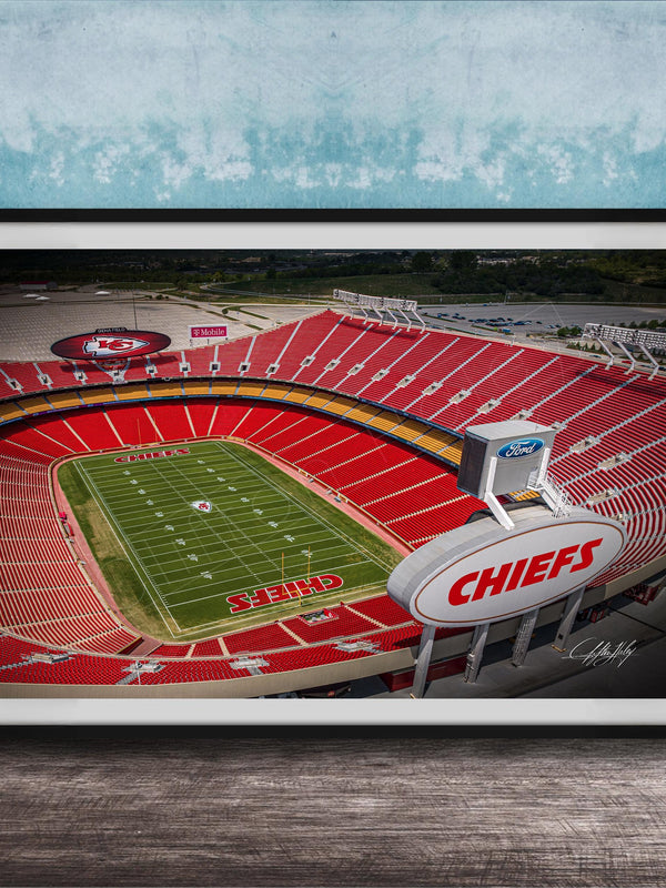 The image is a framed photograph of a football stadium, specifically the Kansas City Chiefs stadium, with the team's logo prominently displayed on the field.