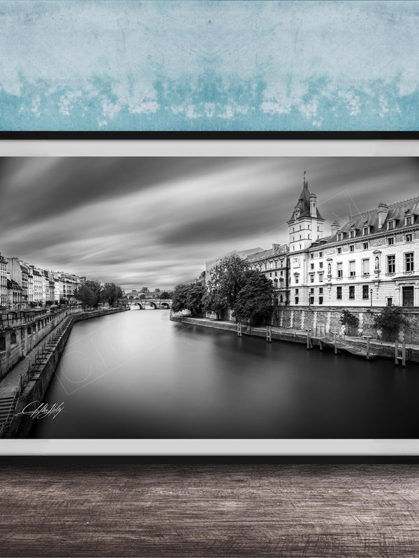 A black and white photograph of a cityscape with a river running through it, featuring a tall building with a clock tower in the background.