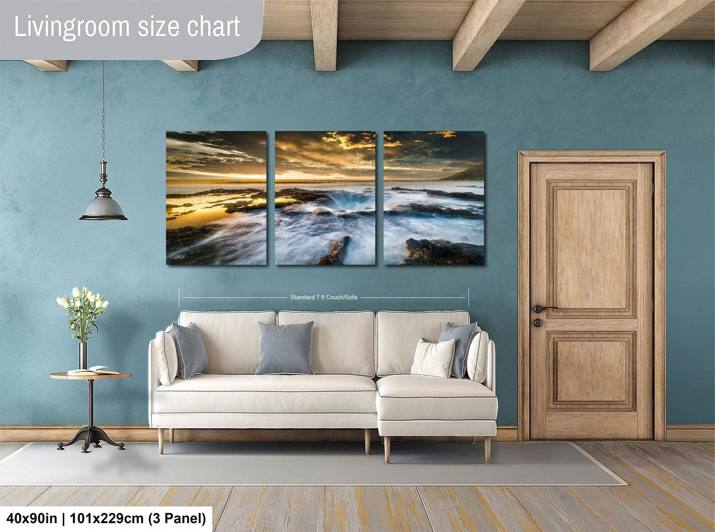 The image is a living room with a large wall art piece depicting a serene landscape of a beach at sunset. The art piece is divided into three panels, each showcasing different aspects of the beach scene. The living room has a white sofa and a wooden door, creating a cozy and inviting atmosphere.