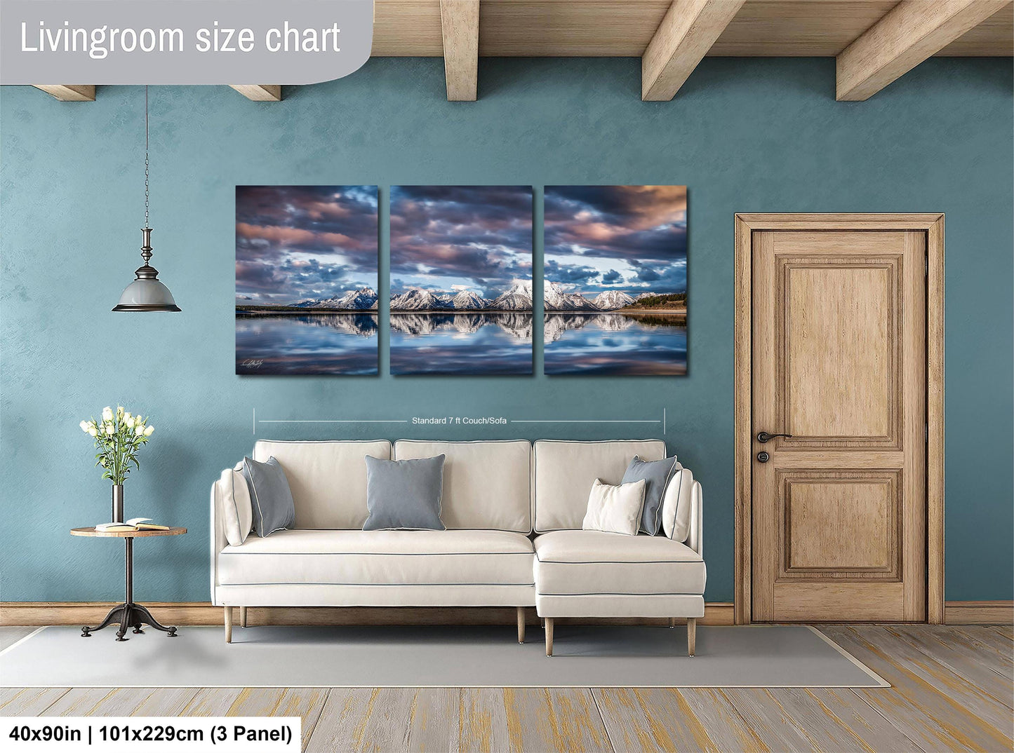 The image is a living room with a large, three-panel landscape painting hanging on the wall. The painting depicts a serene mountain lake scene with a cloudy sky. The room has a white sofa and a wooden door, creating a cozy and inviting atmosphere.