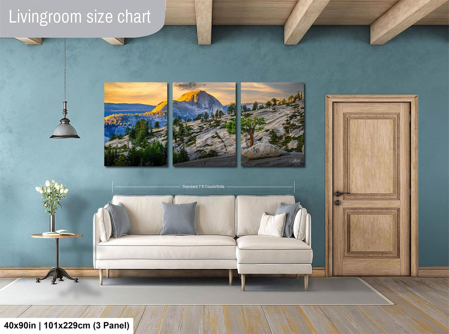 The image is a living room with a large wall art piece depicting a scenic mountain landscape. The art piece is divided into three panels, each showcasing different aspects of the mountain scenery. The living room has a white sofa and a wooden door, creating a cozy and inviting atmosphere.