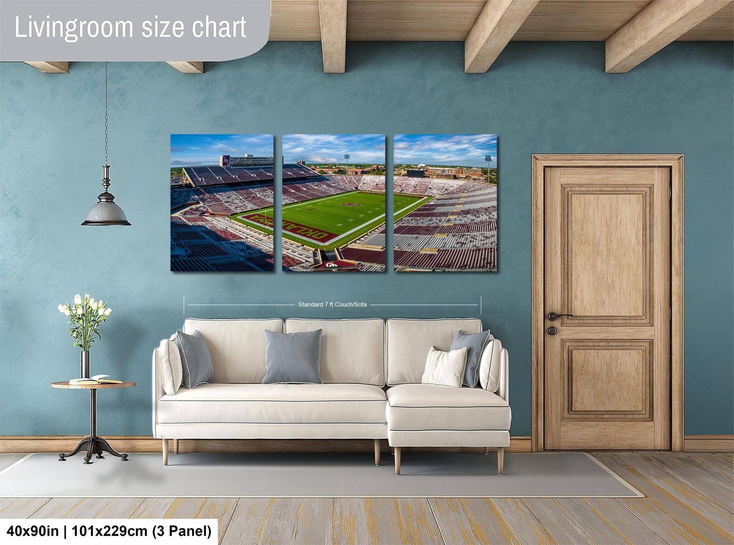 The image is a living room with a large wall-mounted painting depicting a stadium. The painting is divided into three panels, each showing different parts of the stadium. The room has a white sofa, a wooden door, and a small table with a vase of flowers. The painting is approximately 40 inches wide and 101.29 cm tall, with a 3-panel arrangement.