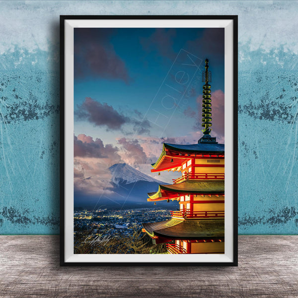 A framed photograph of a traditional Japanese pagoda, with a mountain range visible in the background, set against a blue sky with clouds.