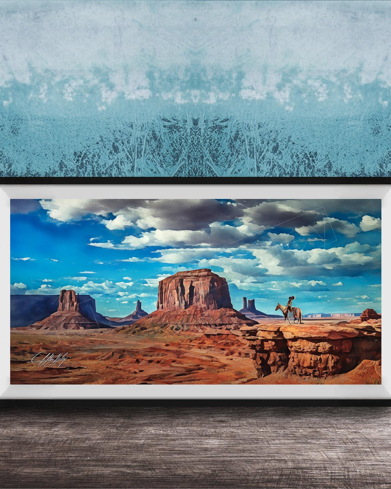 A framed painting depicting a scenic desert landscape with a person riding a horse in the foreground, set against a backdrop of mountains and a blue sky with clouds.
