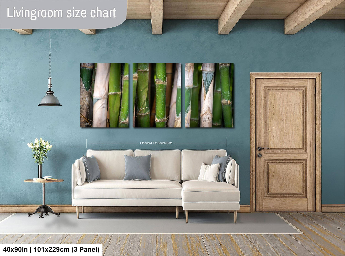 The image is a living room with a large wall art piece depicting a row of bamboo stalks. The art piece is mounted above a white sofa, and there is a wooden door and a small table with a vase of flowers nearby. The living room has a blue wall and wooden beams, creating a cozy and inviting atmosphere.