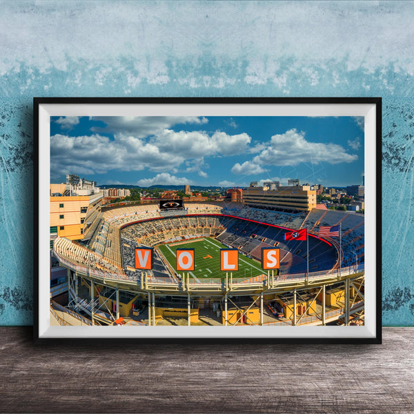 A framed photograph of a football stadium with the word "VOLS" prominently displayed, set against a blue sky with clouds.