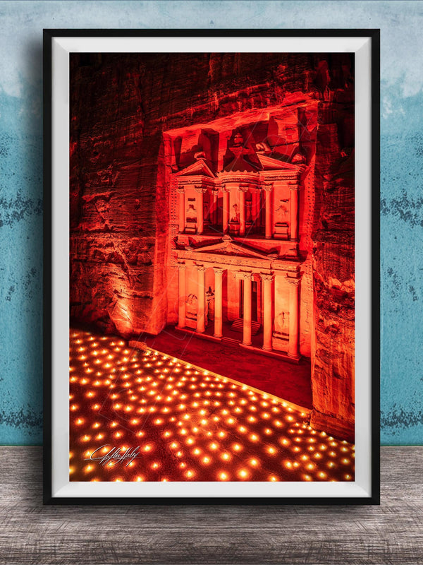The image is a framed photograph of a large, illuminated structure, possibly a temple or monument, with a red and orange glow illuminating the scene. The photograph is set against a blue wall, creating a striking contrast between the illuminated structure and the surrounding environment.