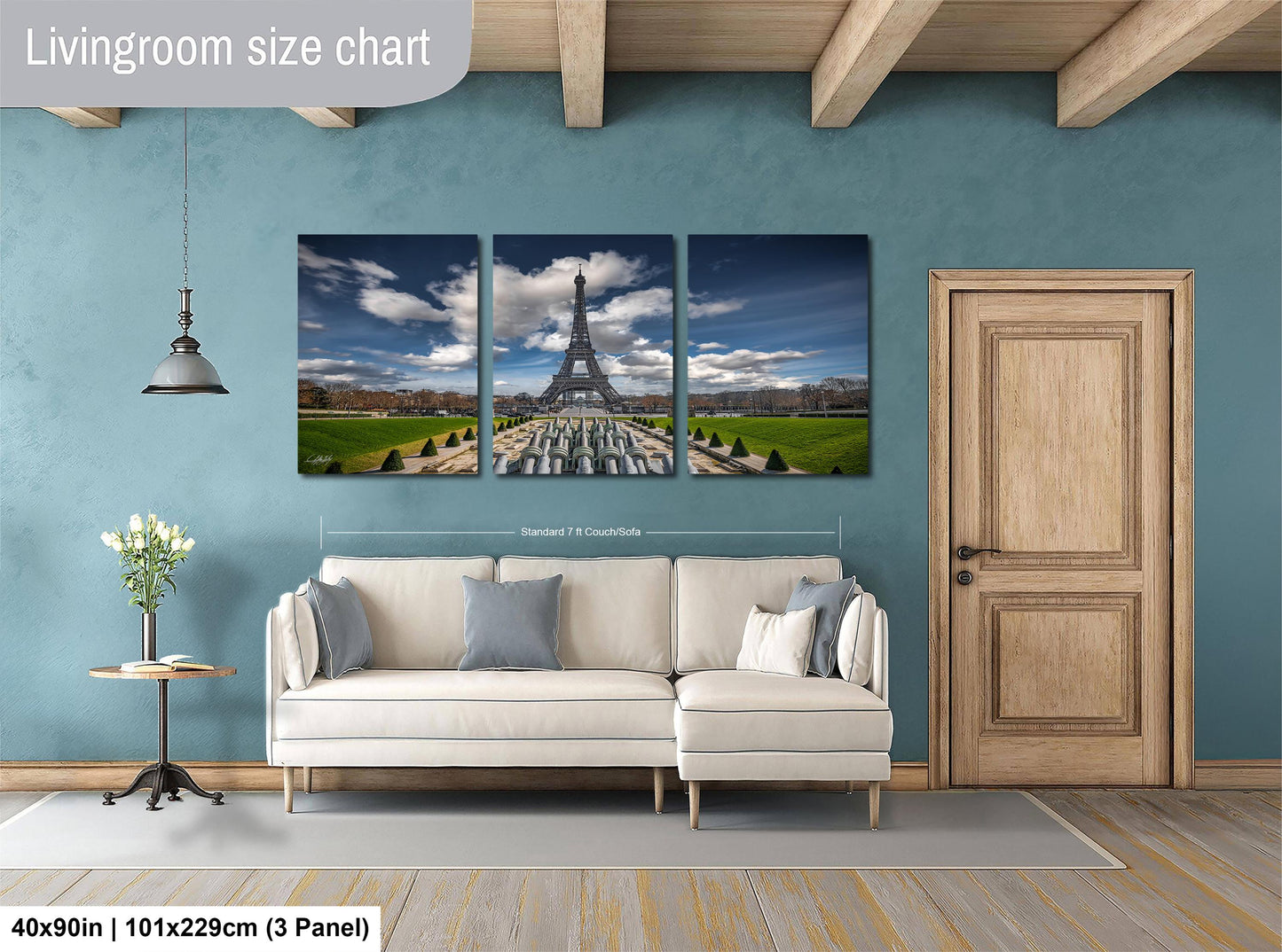 The image is a living room with a large wall art depicting the Eiffel Tower in Paris. The wall art is divided into three panels, each showing different views of the iconic landmark. The living room has a white sofa and a wooden door, creating a cozy and inviting atmosphere.