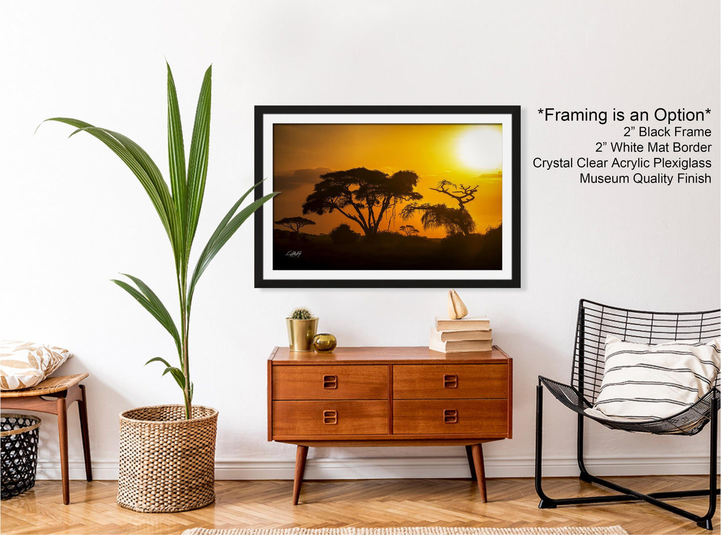a framed photograph of a sunset over a landscape, hanging on a wall in a room with a wooden dresser, a wicker basket, and a black chair.