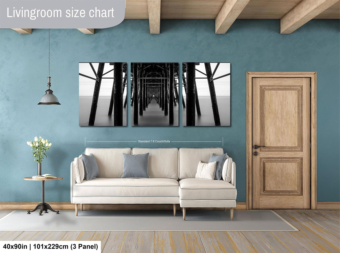 The image is a living room with a white sofa, a wooden door, and a large wall art piece depicting a long pier or walkway.