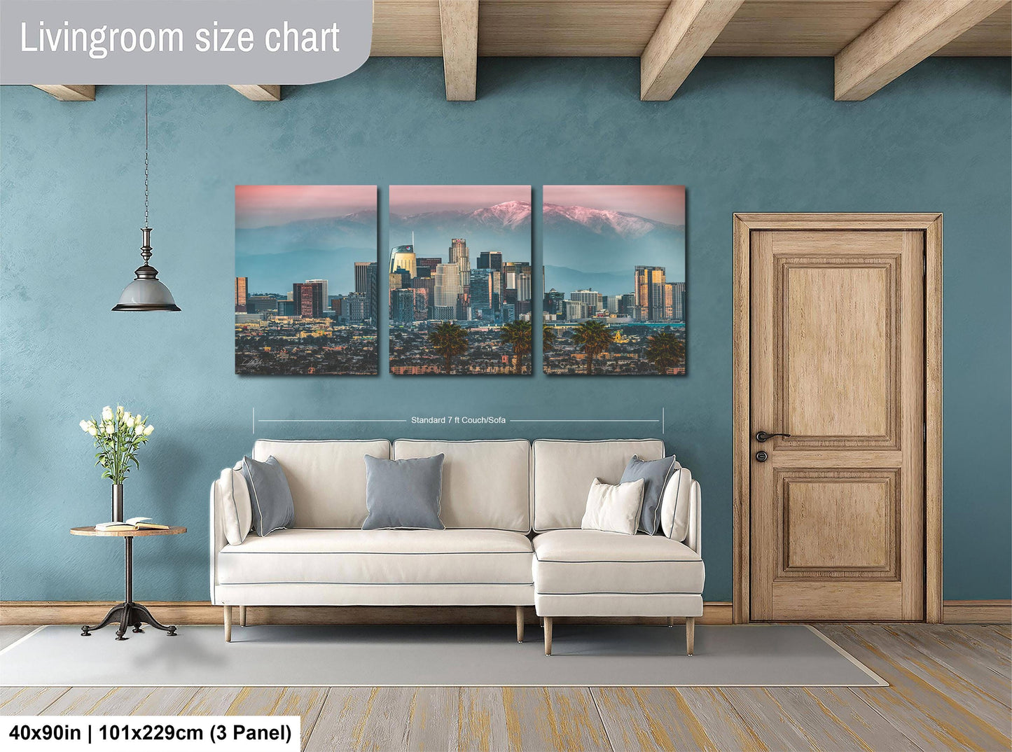 The image is a living room with a large wall art depicting a city skyline at sunset. The wall art is divided into three panels, each showing a different part of the cityscape. The room has a white sofa, a wooden door, and a wooden floor. The wall art is approximately 40 inches wide and 101.29 cm tall, with a 3-panel layout.