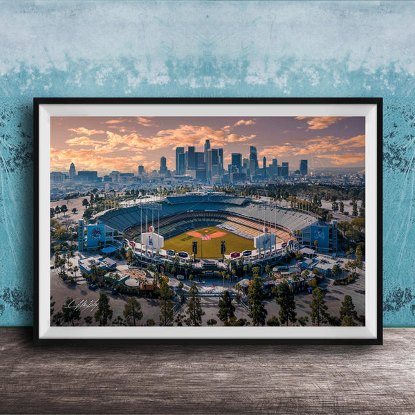 An aerial view of a baseball stadium with the city skyline in the background, framed in a black frame and displayed on a wooden surface.
