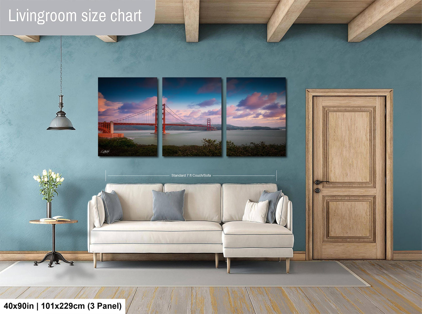 The image is a living room with a large, three-panel, landscape painting of the Golden Gate Bridge hanging on the wall. The painting depicts the bridge at sunset, with the sky filled with clouds and the bridge illuminated by the warm, golden light. The room is furnished with a white sofa and a wooden door, creating a cozy and inviting atmosphere.