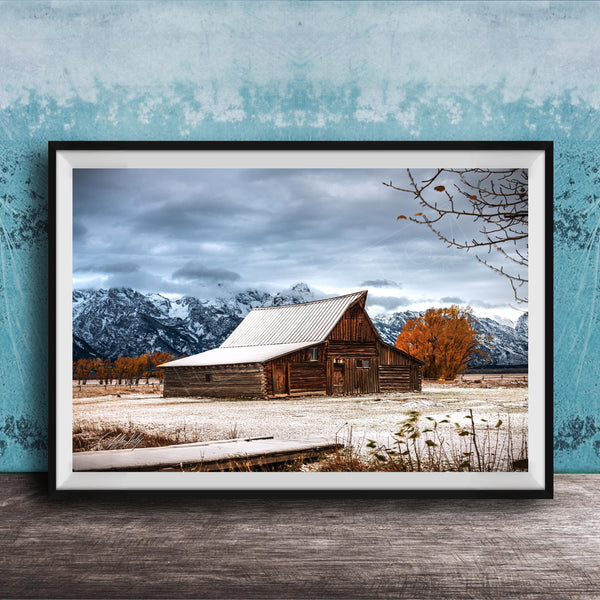 A rustic wooden barn stands in a snowy landscape, with snow-capped mountains in the background and a wooden walkway leading up to the barn.