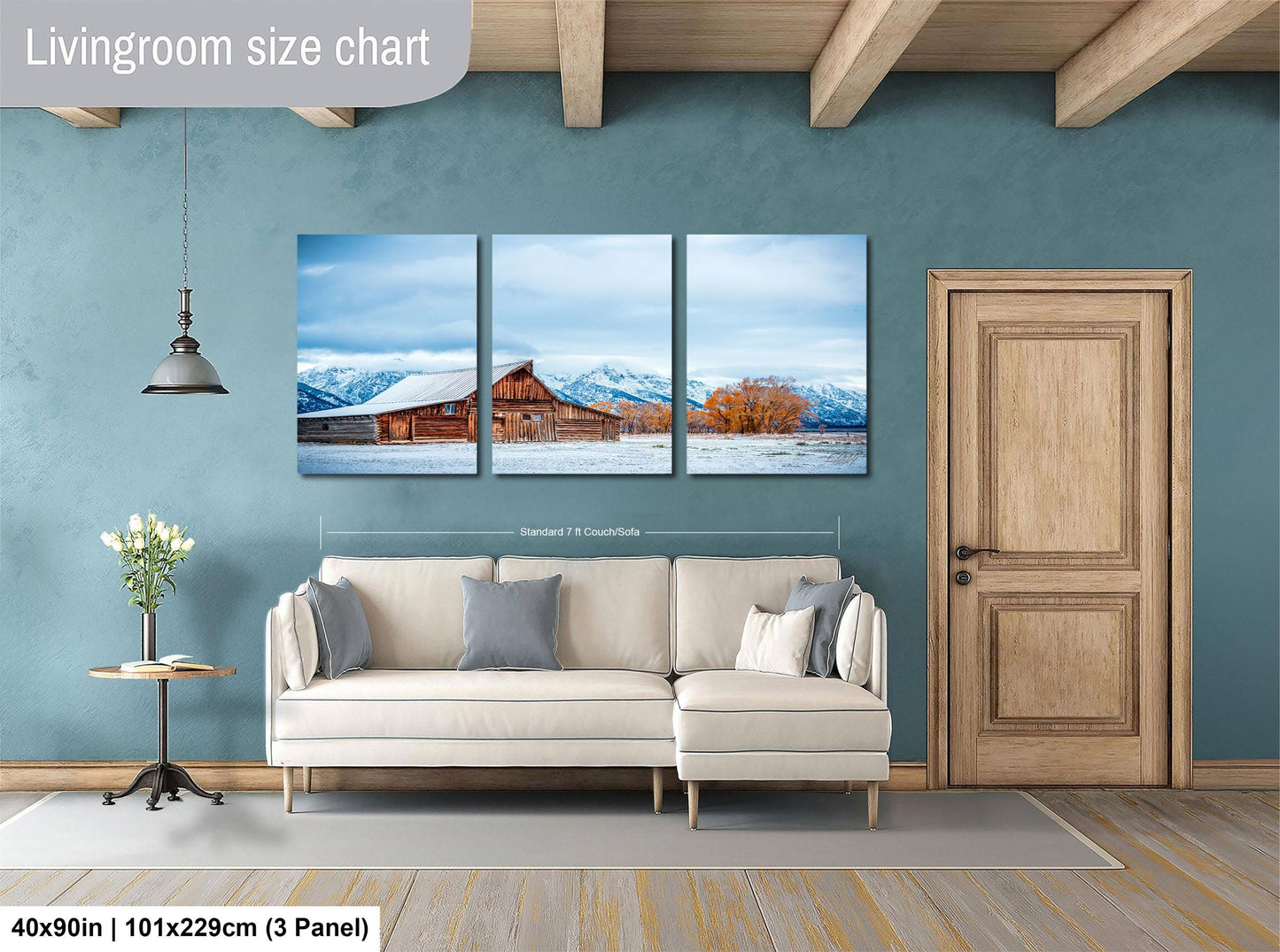 The image is a living room with a large painting of a snowy mountain landscape hanging on the wall. The painting is divided into three panels, and the room has a white sofa, a wooden door, and a small table with a vase of flowers.