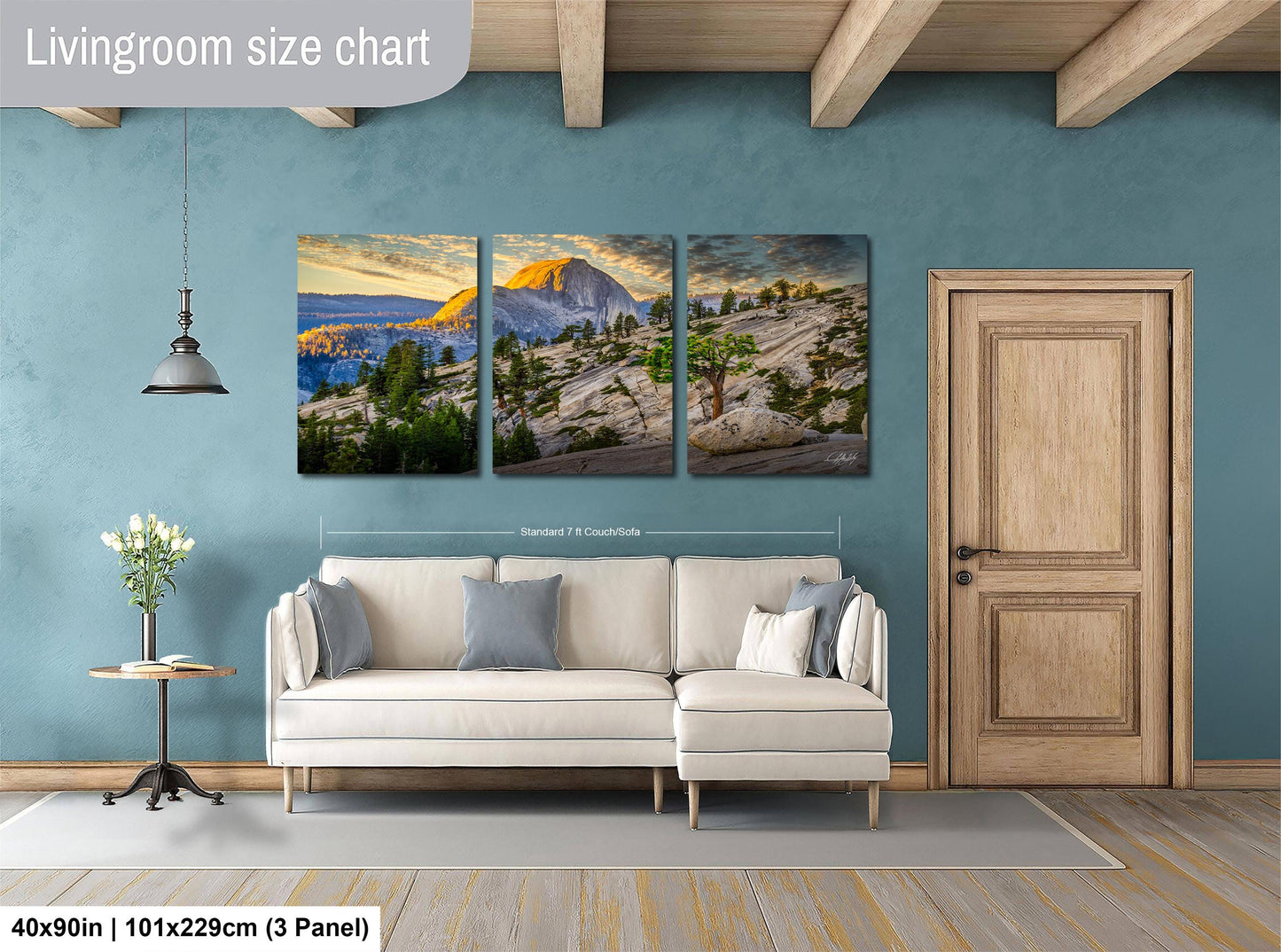 The image is a living room with a large wall art depicting a scenic mountain landscape. The wall art is divided into three panels, each showcasing different aspects of the mountain scenery. The living room has a white sofa and a wooden door, creating a cozy and inviting atmosphere.