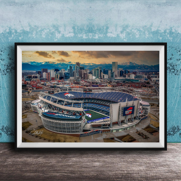 The image is an aerial view of a large sports stadium, likely a football stadium, with the city skyline in the background.