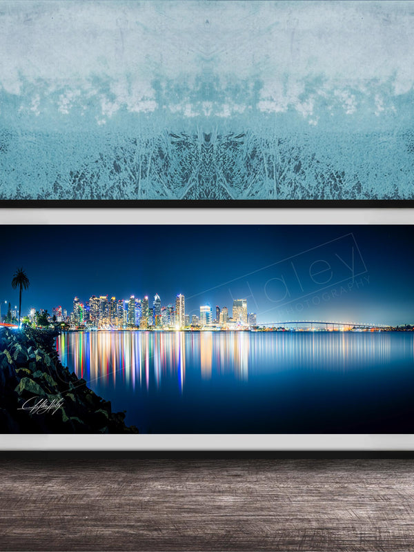 A framed photograph of a city skyline at night, with the city's lights reflected in the water below.