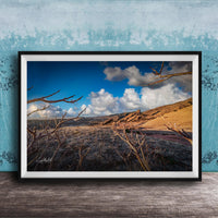 A framed photograph depicting a desert landscape with a blue sky, clouds, and a dry, barren terrain.