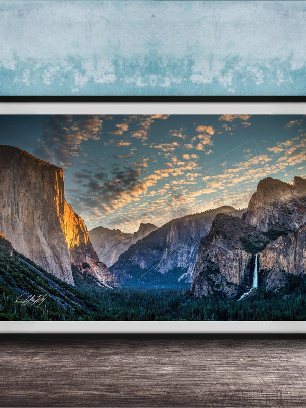 The image is a framed photograph of a breathtaking mountainous landscape, with towering cliffs, a waterfall, and a vibrant sky filled with clouds.