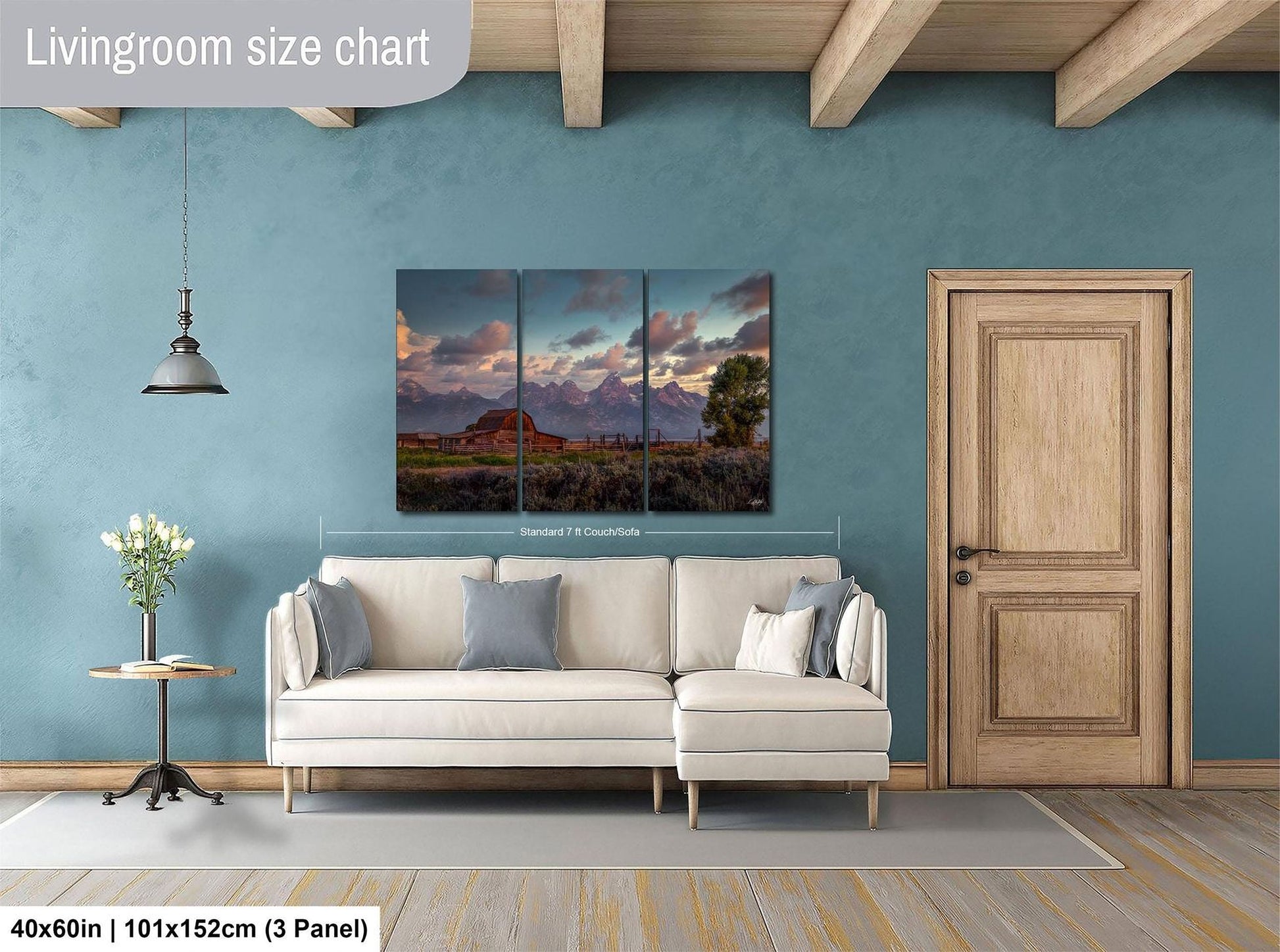 The image is a living room with a large, three-panel landscape painting hanging on the wall. The painting depicts a scenic mountain landscape with a barn and trees. The room has a white sofa and a wooden door, creating a cozy and inviting atmosphere.