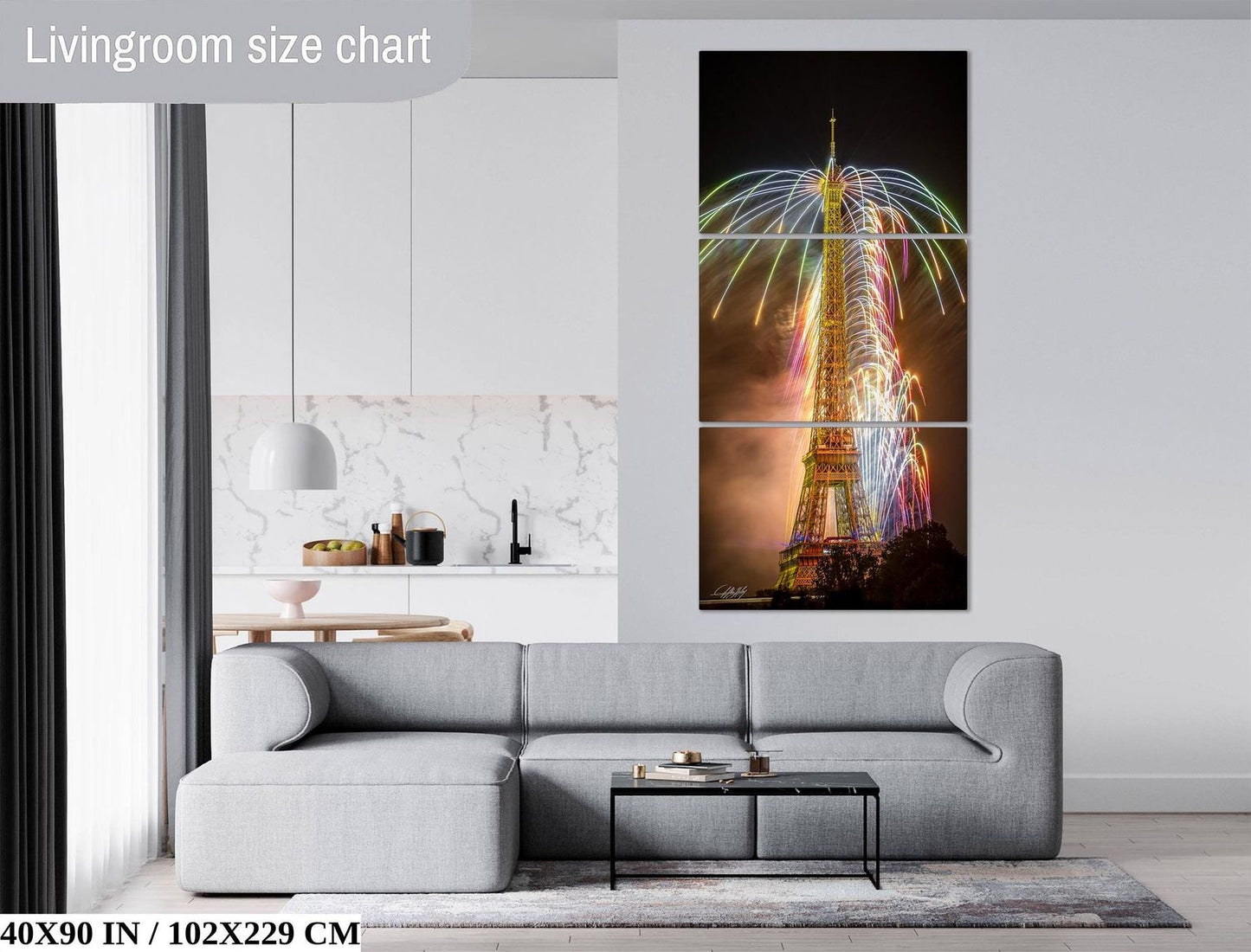The image is a living room with a gray sofa and a coffee table in front of it. Above the sofa, there is a large, colorful painting of the Eiffel Tower. The painting is a triptych, with two panels on either side of the central image. The wall behind the sofa has a white marble finish, and there is a window in the background.
